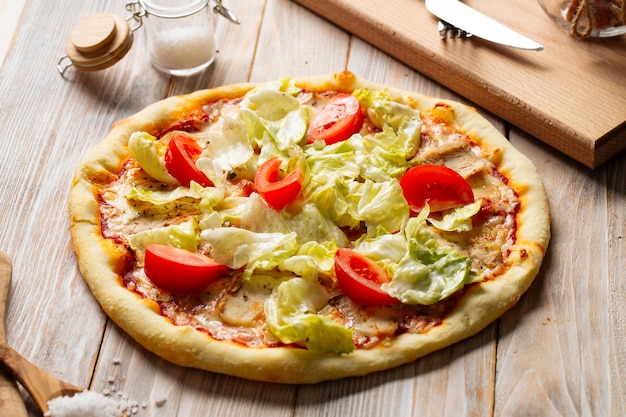 Seitenansicht auf Hühnchen-Caesar-Pizza mit Tomaten und Salat
