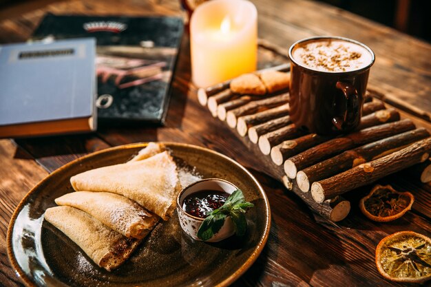 Seitenansicht auf köstlichen wärmenden cappuccino-kaffee mit zimt in einer tasse auf dem holzbrett und pfannkuchen