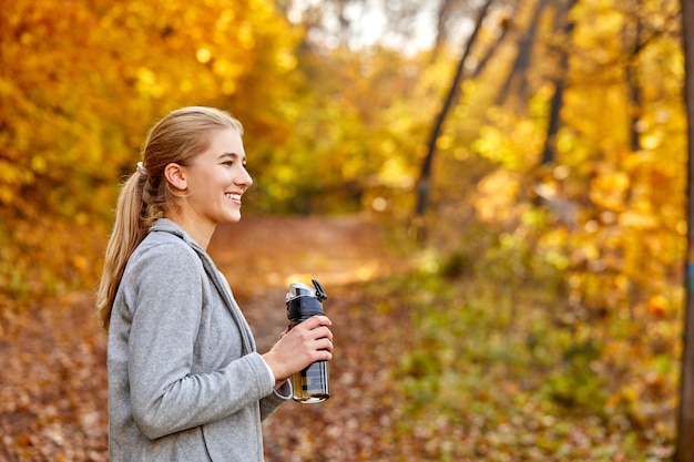 Seitenansicht auf lächelnde blonde Frau, die frisches Wasser in der Natur trinkt, machen Sie eine Pause beim Joggen, Laufen. Lächeln