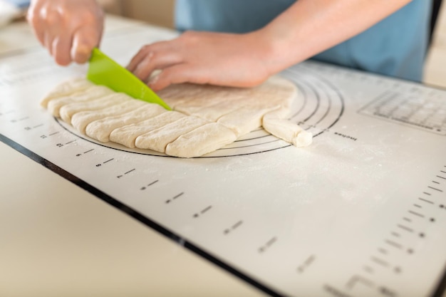 Seitenansicht beim Schneiden von Weizenteig auf einer Backmatte mit Markierungen mit einem Plastikmesser auf dem Kopierraum des Küchentisches