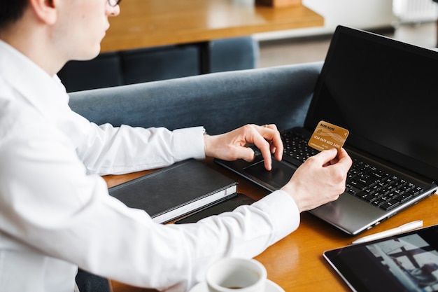 Seitenansicht beschneiden Hände mit einer goldenen Kreditkarte und einem Laptop.