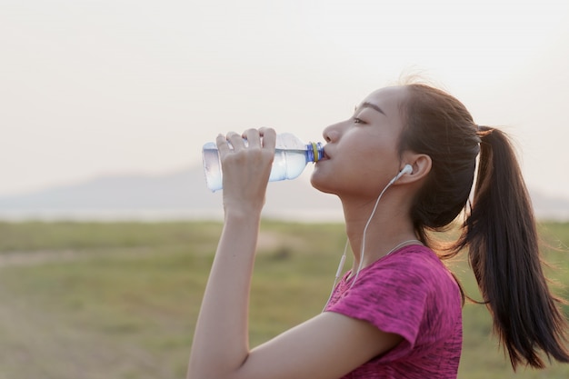 Seitenansicht der asiatischen Fitness-Sportlerinnen mit Trinkflaschenwasser und Entspannung nach einem Training oder Laufen im Sommer bei Sonnenuntergang oder Sonnenaufgang. Konzept Wellness und Lifestyle