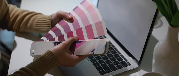 Seitenansicht der Designerhände, die Farbe vom Farbfeld auswählen, während sie mit Laptop im Heimbüro arbeiten