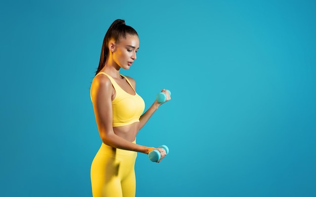 Seitenansicht der fitness-dame, die mit hanteln auf blauem hintergrund trainiert