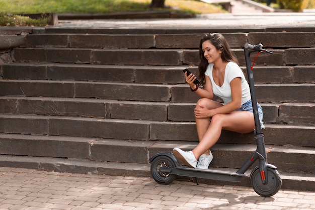 Foto seitenansicht der frau auf stufen mit smartphone neben roller