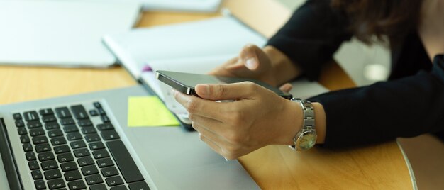 Foto seitenansicht der geschäftsfrau unter verwendung des smartphones beim arbeiten mit büromaterial auf schreibtisch