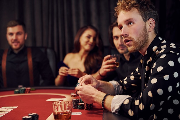 Seitenansicht der Gruppe eleganter junger Leute, die Poker im Kasino zusammen spielen