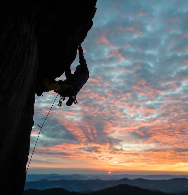 Seitenansicht der Kletterer-Silhouette in Aktion bei Sonnenuntergang über Berggipfeln Wolken bunter Himmel im Hintergrund Kopieren Sie Platz