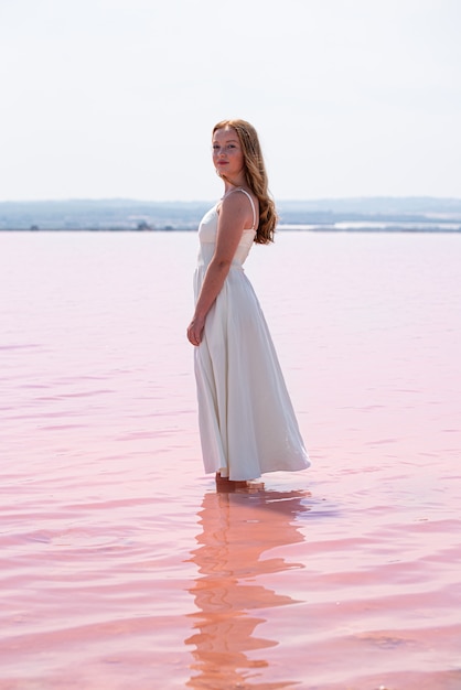 Seitenansicht der niedlichen Teenagerfrau, die weißes Kleid steht, das auf einem erstaunlichen rosa See steht