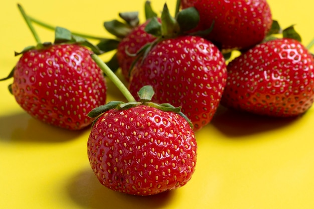 Seitenansicht der saftigen reifen Erdbeeren, die auf einem hellgelben Hintergrund liegen. Gesunde und leckere Beeren, vegetarisches Essen, gesundes Essen