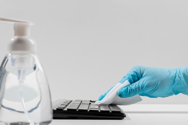 Foto seitenansicht der tastatur, die von hand mit einem chirurgischen handschuh desinfiziert wird