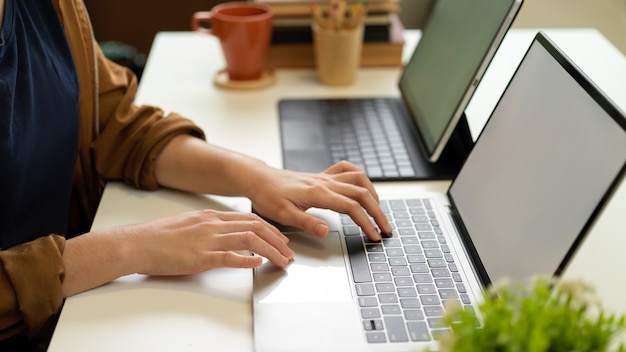 Seitenansicht der weiblichen Hand, die auf Laptoptastatur auf Schreibtisch mit einem anderen Laptop und Büromaterial tippt