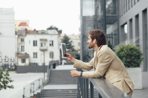 Seitenansicht des attraktiven Mannes mit Bart, der auf Balkon mit digitalem Tablett steht und Videogespräch hat