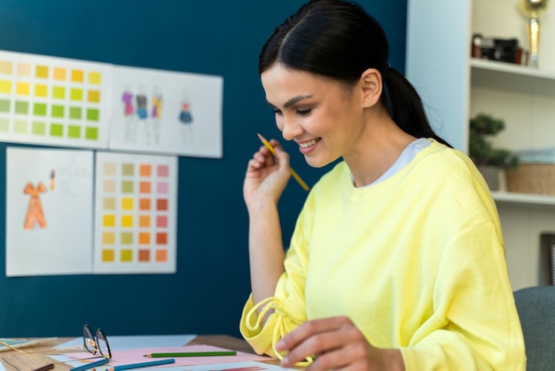 Seitenansicht des attraktiven talentierten Designers, der sich auf das Erstellen von Skizzen im modernen Studio konzentriert, während er mit Papier und Bleistift am Tisch sitzt