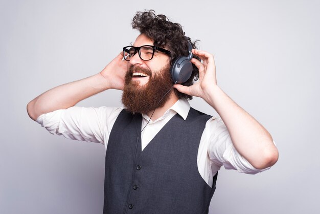 Seitenansicht des bärtigen Hipster-Mannes im Anzug, der Musik an Kopfhörern lehnt.