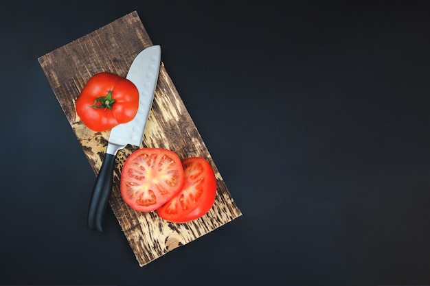 Seitenansicht des fertigen Gerichts mit frischem Gemüse Hohe Betrachtungswinkel von Tomatenscheiben mit Messer auf Schneidebrett auf dunklem Hintergrund