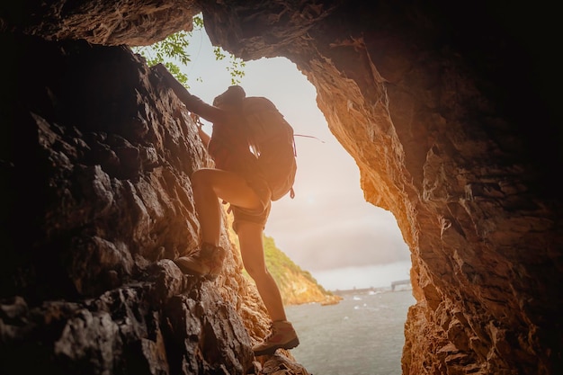 Seitenansicht des Frauenwanderers, der bei Sonnenuntergang auf der Klippe in der Höhle klettert. Frau, Wandern, Wanderer, Berg, Höhle, Aktivitätskonzept.