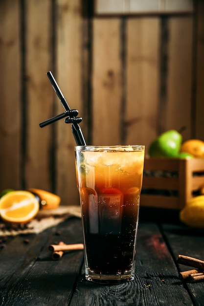 Seitenansicht des Glases des Long Island-Cocktails mit einem schwarzen Strohhalm auf dem hölzernen Hintergrund, vertikal, Seitenansicht