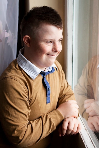 Foto seitenansicht des glücklichen jungen mit down-syndrom, der durch das fenster aufwirft