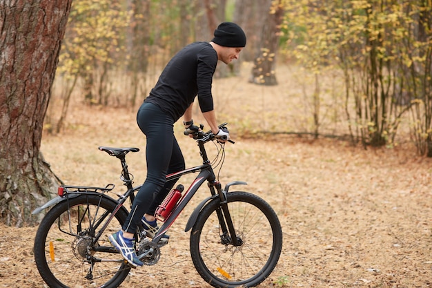 Seitenansicht des hübschen jungen Bikers auf Straße im Wald, Kerl, der um Bäume reitet, frische Luft und schöne Natur genießt