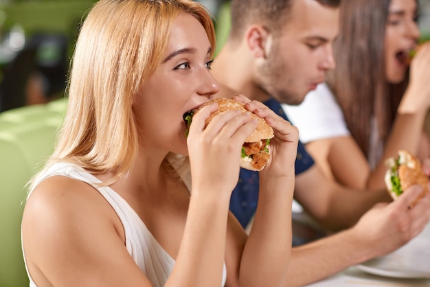 Seitenansicht des hungrigen blonden beißenden großen saftigen Burgers