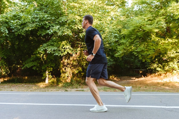 Seitenansicht des jungen hemdlosen Sportlers in den Kopfhörern