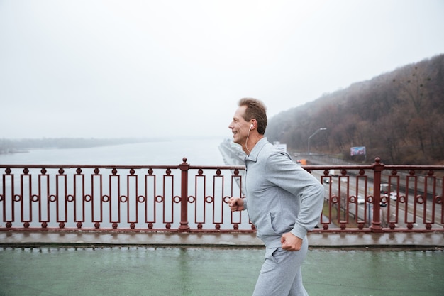 Seitenansicht des Mannes in grauer Sportkleidung, der auf der Brücke läuft