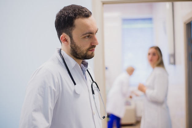 Seitenansicht des nachdenklichen jungen Arztes in der medizinischen Uniform, die dem Patienten zuhört