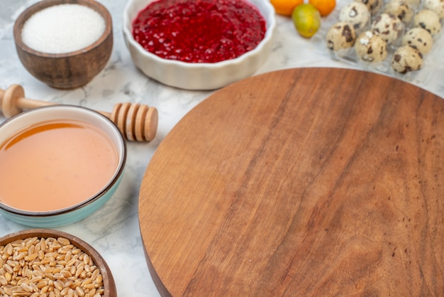 Seitenansicht des runden Holzschneidebretts Marmelade Honig Eier brauner Reis frische Kumquats auf Eishintergrund