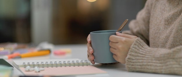 Seitenansicht des Studenten, der Tasse hält, während er am Studiertisch mit Briefpapier sitzt