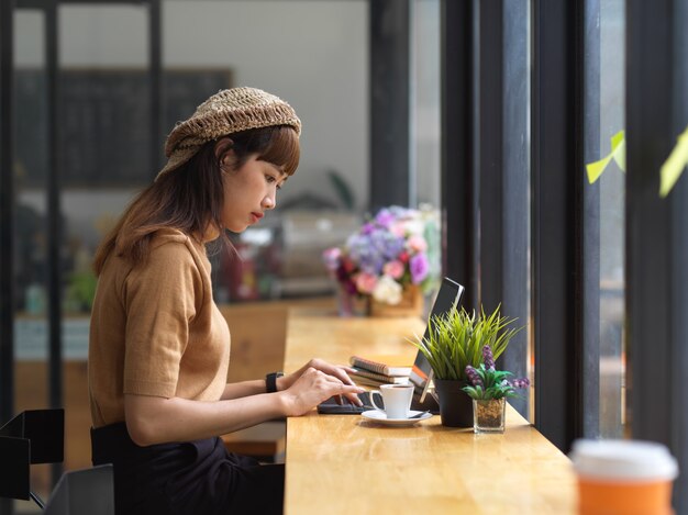 Seitenansicht des weiblichen Teenagers, der Hausaufgaben mit Tablette auf hölzerner Bar im Café tut