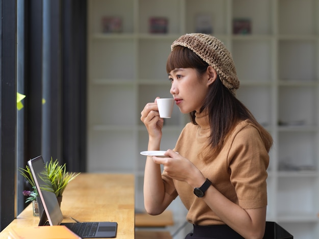 Seitenansicht des weiblichen Teenagers entspannte sich mit dem Kaffeetrinken, während mit Tablette im Café gearbeitet wurde