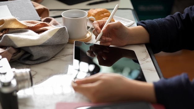 Foto seitenansicht, eine freiberuflerin, die einen digitalen tablet-touchpad-computer mit stylus-stift an ihrem schreibtisch verwendet.