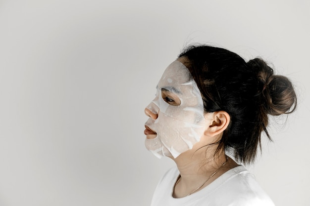 Foto seitenansicht einer asiatischen frau, die ein weißes t-shirt trägt und ihr gesicht mit einer blattmaske bedeckt.