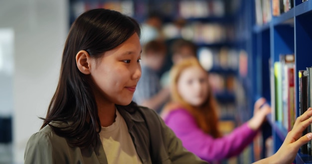 Seitenansicht einer asiatischen Schülerin, die im Bibliotheksregal nach einem Buch sucht