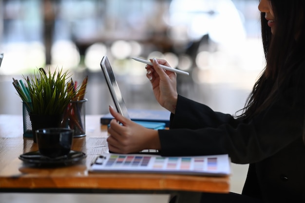 Seitenansicht einer attraktiven jungen Designerin, die an einem Tablet-Computer arbeitet, während sie im Kreativbüro sitzt.