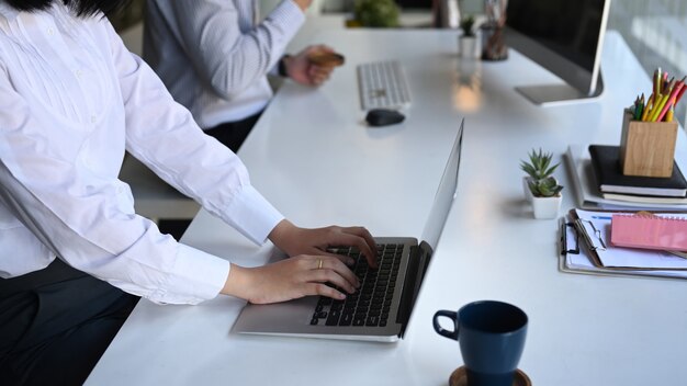 Seitenansicht einer Büroangestellten, die am Laptop arbeitet und mit ihrem Kollegen am Schreibtisch sitzt.