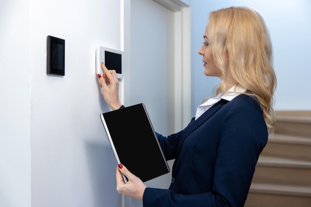 Seitenansicht einer fokussierten Frau, die den Knopf auf einem digitalen Gerät an der Wand drückt