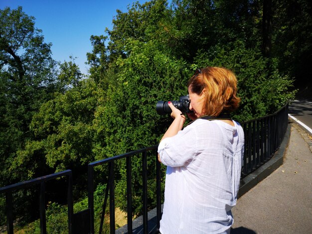 Foto seitenansicht einer frau, die bäume von der straße aus fotografiert