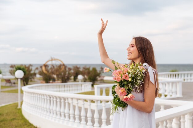 Seitenansicht einer Frau, die Blumen hält und draußen an der weißen Terrasse winkt
