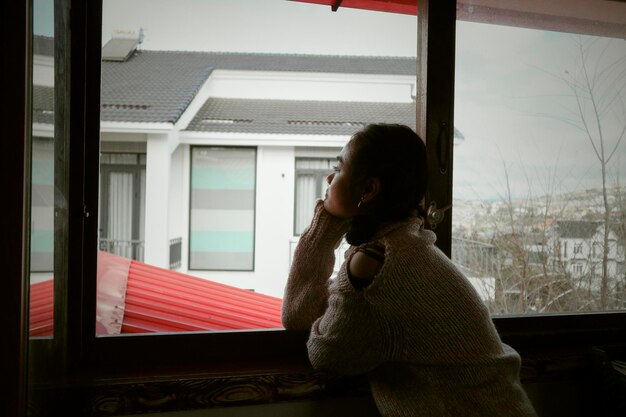 Foto seitenansicht einer frau, die durch das fenster schaut