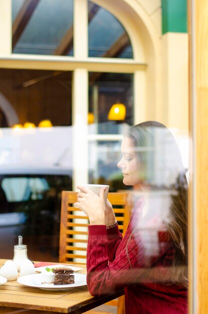 Foto seitenansicht einer frau, die ein glas auf einem tisch im café trinkt