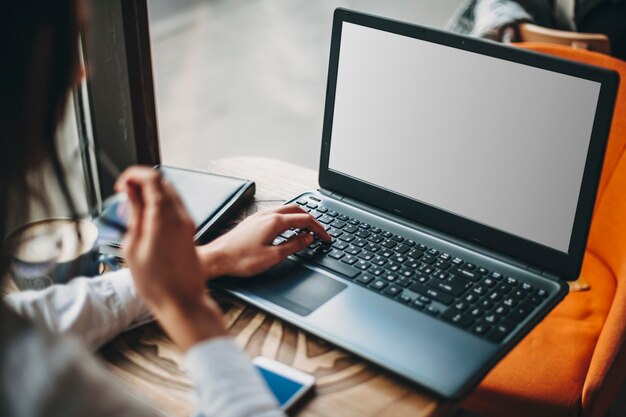 Seitenansicht einer Frau, die in einem Café sitzt, während sie online auf einem Laptop einkauft.