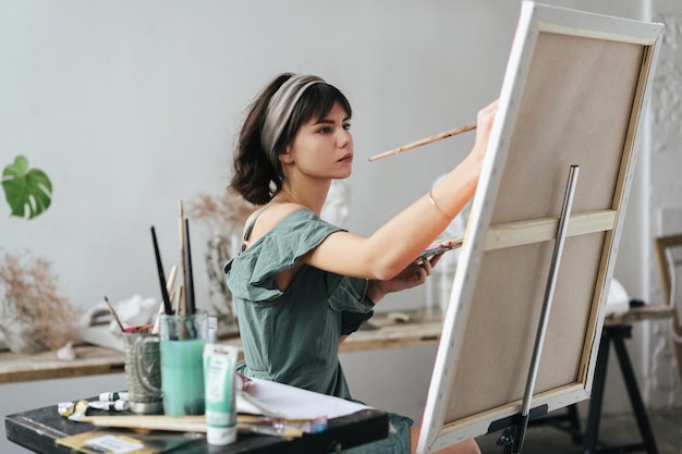 Seitenansicht einer Frau, die in einem Kunststudio auf Leinwand malt