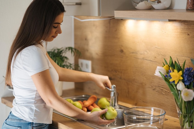 Seitenansicht einer Frau, die Äpfel wäscht und Obst und Gemüse für einen gesunden hausgemachten Saft zubereitet