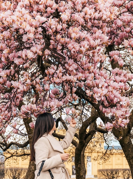 Seitenansicht einer Frau, die unter einem wunderschönen rosafarbenen Magnolienbaum in Zagreb, Kroatien, steht.