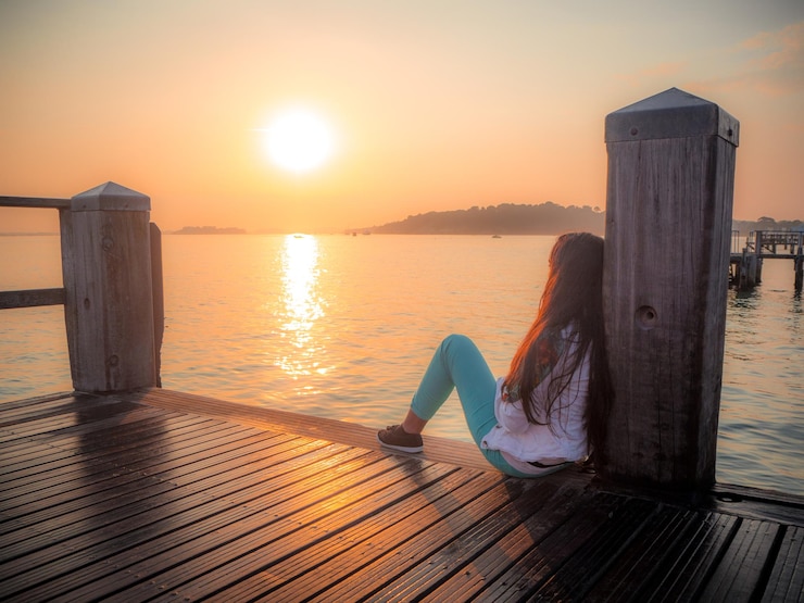 Foto seitenansicht einer frau, die während des sonnenuntergangs auf dem steg über dem meer gegen den himmel sitzt