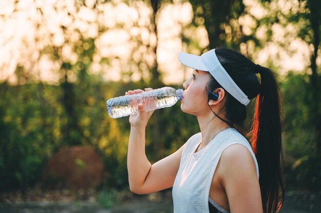 Seitenansicht einer Frau, die Wasser aus einer Flasche gegen Bäume trinkt