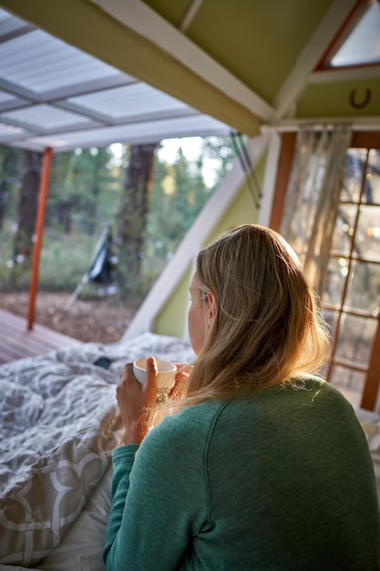 Foto seitenansicht einer frau, die zu hause auf dem bett sitzt und ein getränk hält