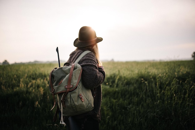 Seitenansicht einer Frau mit Rucksack, die bei Sonnenuntergang auf dem Land gegen den Himmel steht